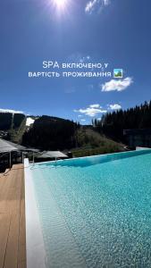 a blue swimming pool with the sun in the sky at SAVOIE Apartments Bukovel in Bukovel