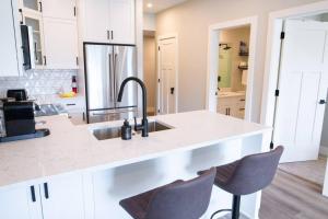 a kitchen with white cabinets and a sink and two chairs at New 1 Bed Condo with Mtn Views in Harrison Hot Springs +49 photos