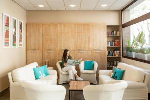 una mujer sentada en una silla leyendo un libro en Hotel Domomea, en Alghero