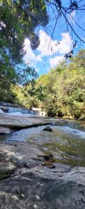 a river with a waterfall in the background with trees at Pousada do Coura in Pouso Alto