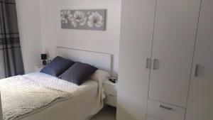 ein weißes Schlafzimmer mit einem Bett mit blauen Kissen in der Unterkunft Apartamento nuevo con piscina y amplio balcon in Sant Carles de la Ràpita