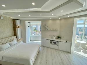 a bedroom with a large white bed and a kitchen at Кращі панорамні квартири Sky House у центрі Вінниці Безключовий доступ! in Vinnytsya