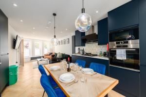 a kitchen and dining room with a wooden table and blue cabinets at The Old Kiosk - Luxe 4 Bed House - Roath Park in Cardiff