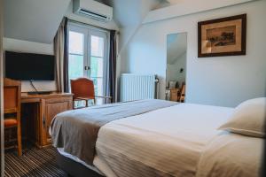 een slaapkamer met een bed, een bureau en een televisie bij Hotel Les Eleveurs in Halle