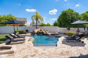 a pool with chairs and an umbrella in a backyard at Two Separate Game Rooms, Heated Pool, Spa, B-ball Court in Mesa