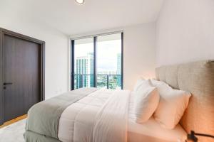 a white bedroom with a bed and a large window at Stylish Condo near Bayside Park: Amazing Views Await in Miami
