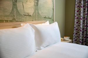 1 cama con almohadas blancas y una pintura en la pared en President Hotel, en Londres