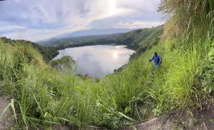 a man walking on a hill overlooking a lake at Roots cottages and campsite Ntanda crater lake 