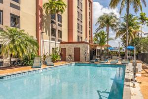 uma piscina com cadeiras, palmeiras e edifícios em Hampton Inn Miami-Airport West em Miami