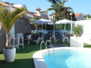 a pool with chairs and umbrellas next to a house at Beach Boys Resort Men Only solo hombres in Maspalomas