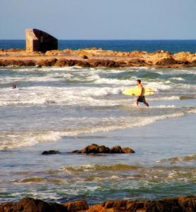 un hombre caminando hacia el océano con una tabla de surf amarilla en ZAG Coliving Punta del este, en Punta del Este