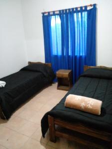 two beds in a room with blue curtains at La Soñada in Malargüe
