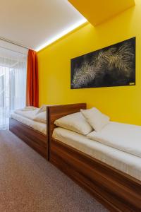 two beds in a room with a yellow wall at Hostel Mayer Superior Veszprém in Veszprém