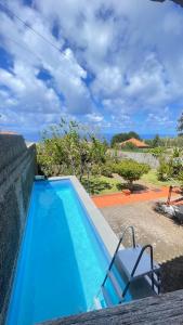 a blue swimming pool with a chair and the ocean at Cantinho da Ponta do Pargo in Ponta do Pargo