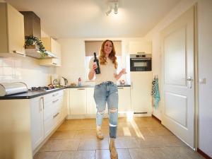 a woman standing in a kitchen holding a bottle at Spledid villa with sauna and whirlpool in Limburg in Roggel