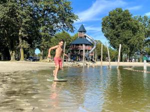 Ein Mann steht auf einem Surfbrett im Wasser mit einem Spielplatz in der Unterkunft Villa Buitenhof De Leistert 6 in Roggel