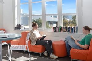 duas mulheres sentadas em cadeiras numa biblioteca a ler em Jailhouse Accommodation em Christchurch