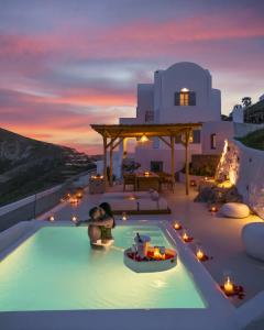 una pareja bañándose en una piscina al atardecer en Bluewhite Villa Santorini en Pyrgos