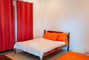 una camera da letto con letto con cuscini arancioni e tende rosse di RedDoorz @ Hergem Siargao Inn a General Luna