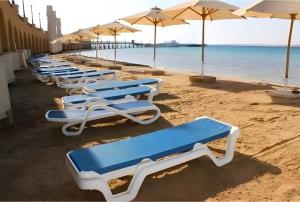 a row of lounge chairs on a beach with umbrellas at Apartman Andalusie in Hurghada