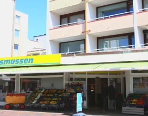 un hombre parado frente a un mercado con frutas y hortalizas en Sueßes Appartement im Zentrum von Westerland in unmittelbarer Strandnähe, en Westerland