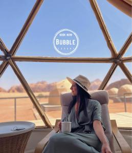 Wadi rum Bubble luxury camp في وادي رم: امرأة تجلس على كرسي مع كوب من القهوة