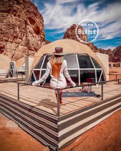 瓦迪拉姆的住宿－Wadi rum Bubble luxury camp，站在帐篷前的木板路上的女人
