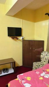 a room with a bed and a chair and a flat screen tv at Dew Drops Guest House in Darjeeling