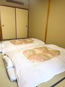 two beds in a room with white sheets at Yoshiike Ryokan in Hakone