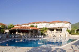 a swimming pool in front of a building with tables and chairs at Hotel Elina in Perdika