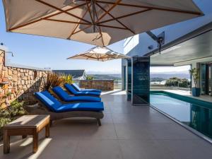 a patio with blue chairs and an umbrella next to a swimming pool at Keurbooms Lagoon Villa in Plettenberg Bay