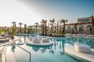 ein Hotelpool mit weißen Stühlen und Palmen in der Unterkunft Europa Beach Hotel & Spa in Hersonissos