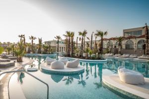 a hotel swimming pool with white chairs and palm trees at Europa Beach Hotel & Spa in Hersonissos