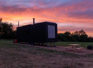 a black tiny house with a picnic table and a sunset at OffGrid Tiny Home W/ View Of South Downs NP in Petersfield