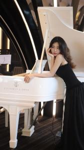 頭頓的住宿－Premier Pearl Hotel Vung Tau，坐在白钢琴上的身着黑色裙子的女人