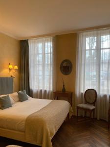 a bedroom with a bed and a chair and windows at The Originals Boutique, Hôtel de la Paix, Beaune (Qualys-Hotel) in Beaune