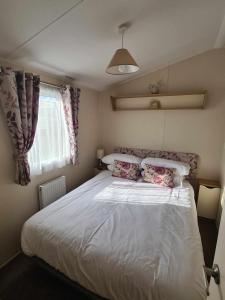 - une chambre avec un lit blanc avec des oreillers et une fenêtre dans l'établissement Happy Days Caravan Primrose Valley, à Filey