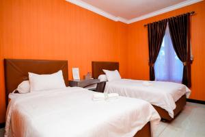twee bedden in een kamer met oranje muren bij Mess Rejeki Redpartner in Sampit
