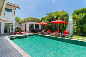 a swimming pool with chairs and umbrellas next to a house at Villa Miro in Seminyak