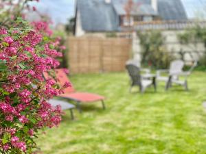 two benches and a table in a yard with pink flowers at La maison des Declos avec parking privé in Bayeux