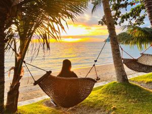 Badladz Beach and Dive Resort في بويرتو غاليرا: امرأة جالسة على أرجوحة تشاهد غروب الشمس