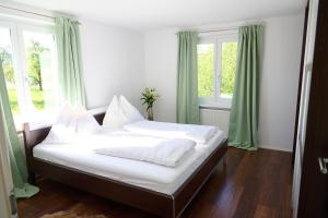 a bed with white sheets and pillows in a room with windows at Naturidyll am See in Fußach