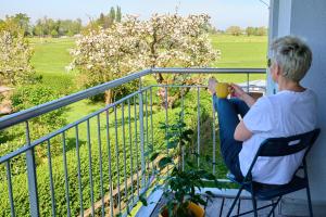 une femme assise sur un balcon buvant une tasse de café dans l'établissement Naturidyll am See, à Fußach