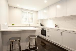 uma cozinha branca com armários brancos e dois bancos em Bayside Retreat em Sydney