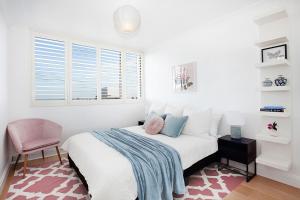 a white bedroom with a bed and a pink chair at Centennial Retreat in Sydney