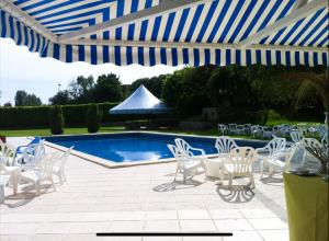 een patio met stoelen en een zwembad met een blauwe en witte parasol bij EXIGEHOME - Bel appartement à 500 m des JOs équitation - Piscine et tennis in Le Chesnay