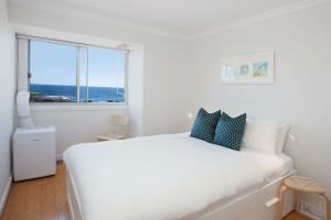 a white bedroom with a large white bed and a window at Ocean view Clovelly in Sydney