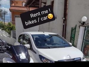 a white car parked in a parking lot with a rent me bikes car sign at Art Studios Benitses in Benitses