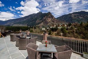 a balcony with a table and chairs and mountains at Sarthak Regency by M K Hospitality,Rangri, Manali,HP,Just 1 kms from Volvo parking in Manāli