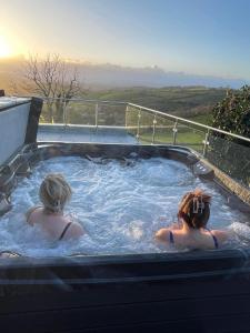 Due donne sono sedute in una vasca idromassaggio di Dog friendly, Roof top hot tub, Panoramic views. a Torquay